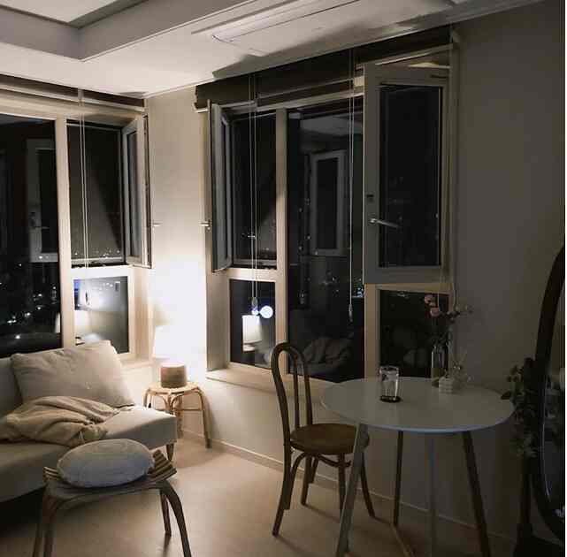 温かみのあるホワイトとナチュラルな木目調のリビング、ソファと丸テーブル、落ち着いた照明が配置された雰囲気のあるインテリア