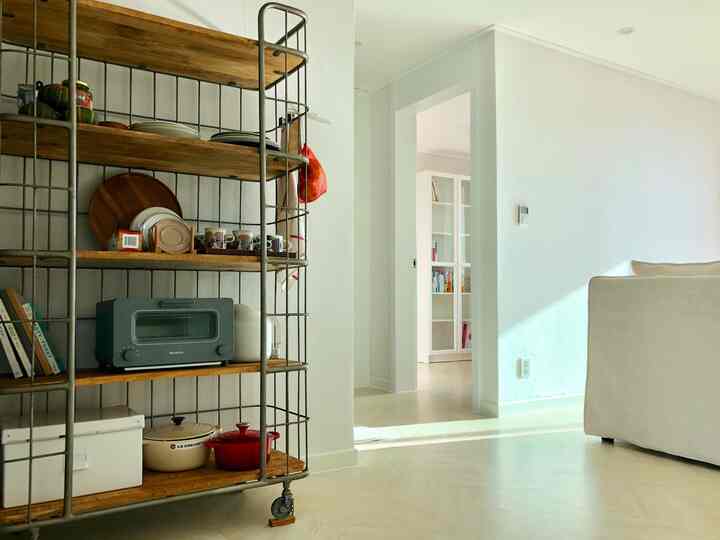 Bright, compact kitchen living space with white walls and sofa, featuring a vintage kitchen cart with wooden shelves and metal frame