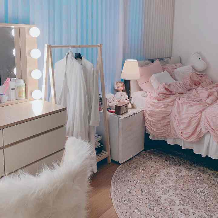 White and pink toned bedroom featuring wooden vanity and clothes rack, with cute decorative elements creating a warm atmosphere