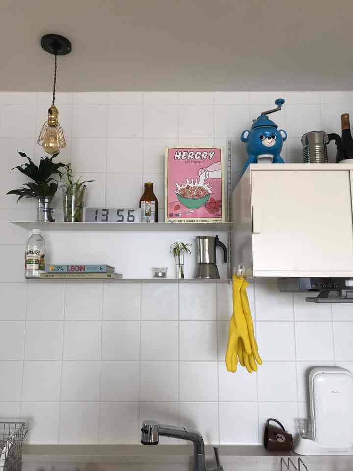A clean kitchen space with white tiled walls, simple shelves, a digital clock, and home cafe accessories arranged neatly