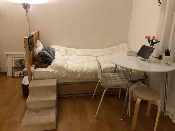 A cozy and practical small bedroom in white and beige tones featuring a bed and round table with seating