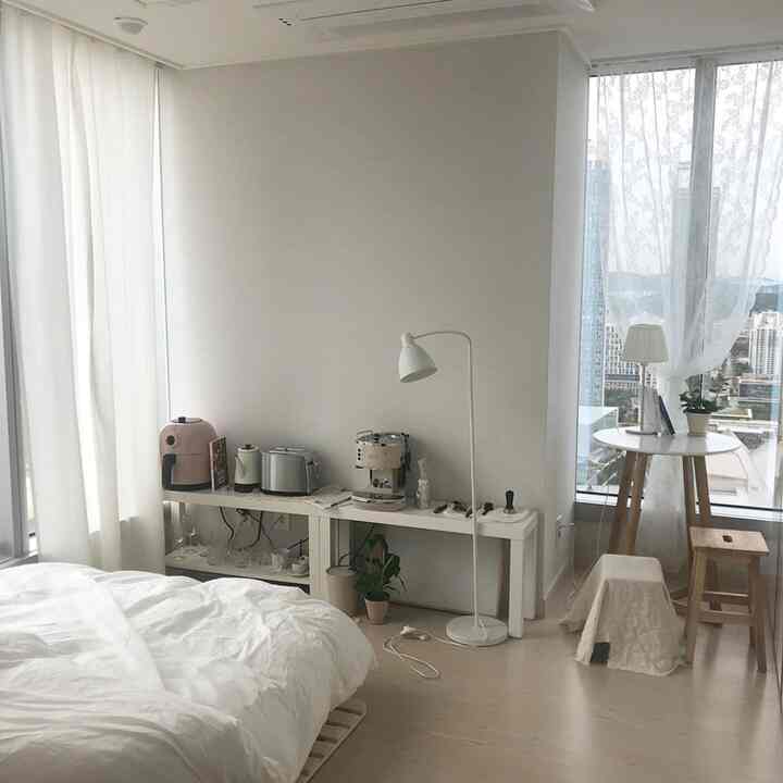 White and natural tone studio apartment with bed and home cafe area featuring stools and a round table in a cozy layout