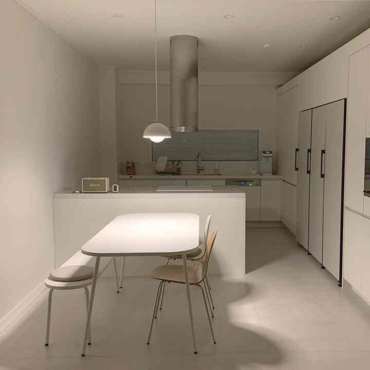白を基調としたシンプルなキッチン、中央にダイニングテーブルと椅子が配置され、ビスポーク冷蔵庫とマシャルスピーカーが印象的な空間