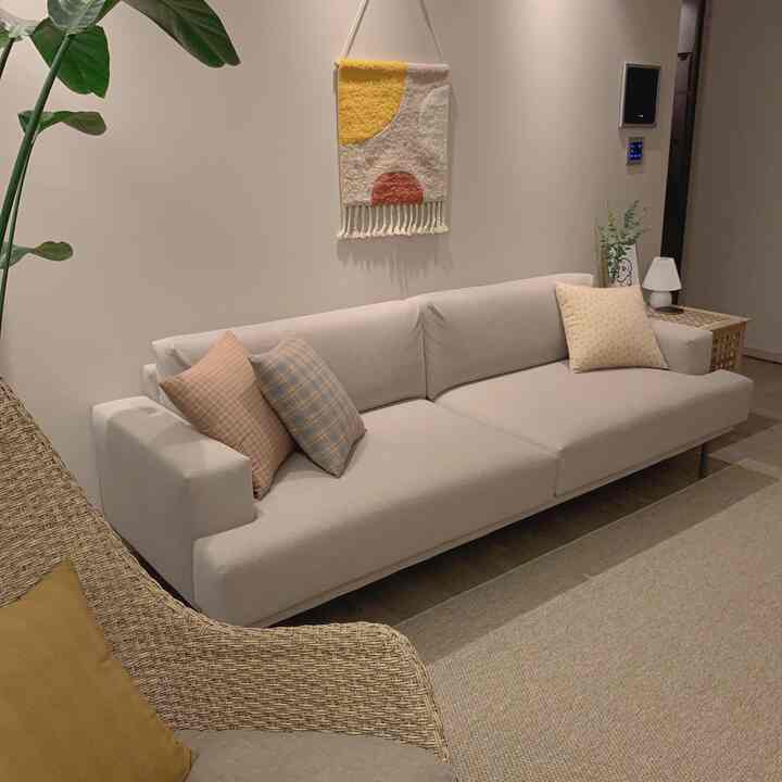 Cozy beige-toned living room featuring a fabric sofa with brown cushions, rattan chair, and wall decor, creating a warm ambiance