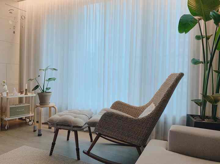 Bright white-toned living room featuring rattan rocking chair with cushions and large leafy plants for a natural and cozy atmosphere