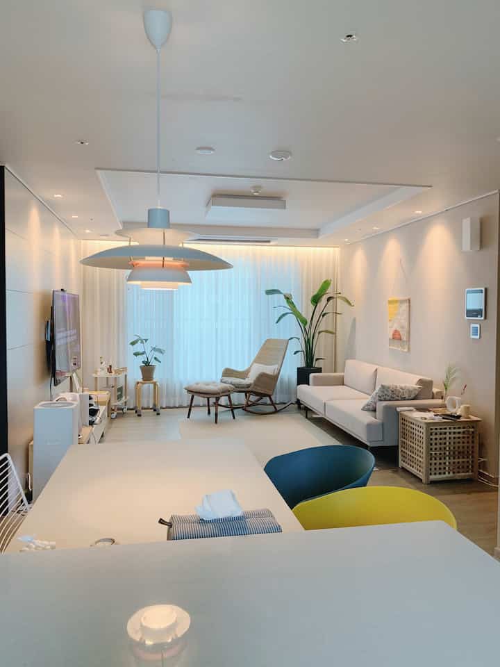 白とベージュの色調のリビング、ソファとラタンのアームチェアが配置されたナチュラルでカフェ風の印象的な空間