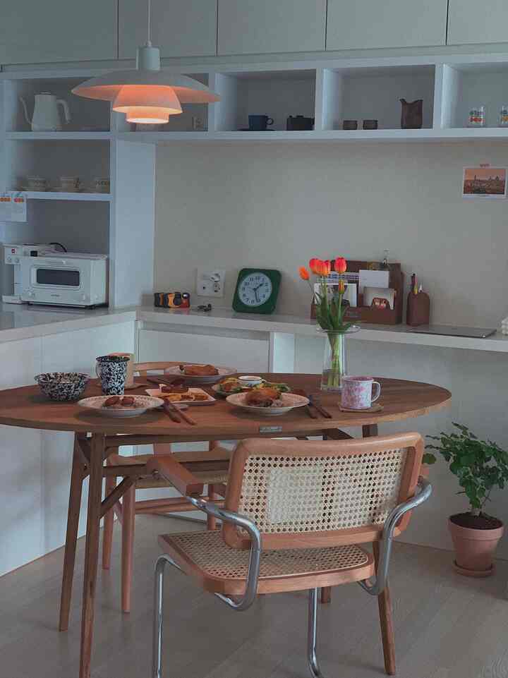 White and brown toned kitchen and dining room featuring a wooden round table and rattan chairs in a cozy dining space