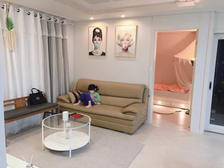 Natural beige-toned living room featuring a brown leather sofa, round coffee table, and an adjacent kids' room creating a warm family space