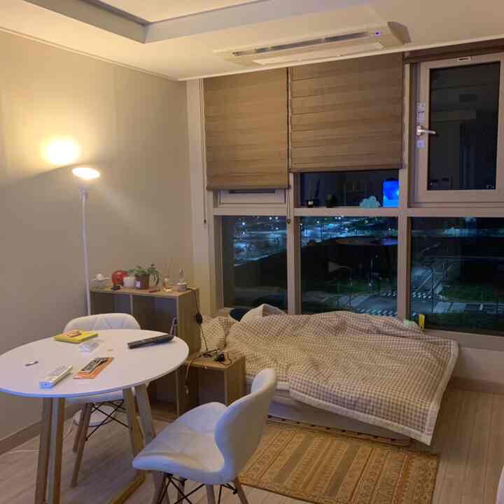 Beige curtains and bed with white dining table and chairs in a compact bedroom-living room, cozy simple modern style space