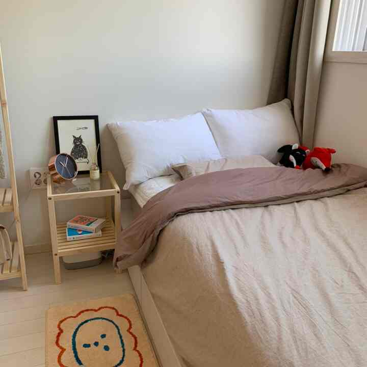 Beige and wood tone bedroom featuring cozy bedding and a wooden nightstand in a snug small room