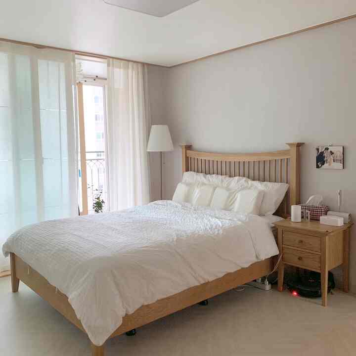 Bright white and natural wood tone bedroom featuring white bedding, curtains, and wooden bed with nightstand in a clean setting