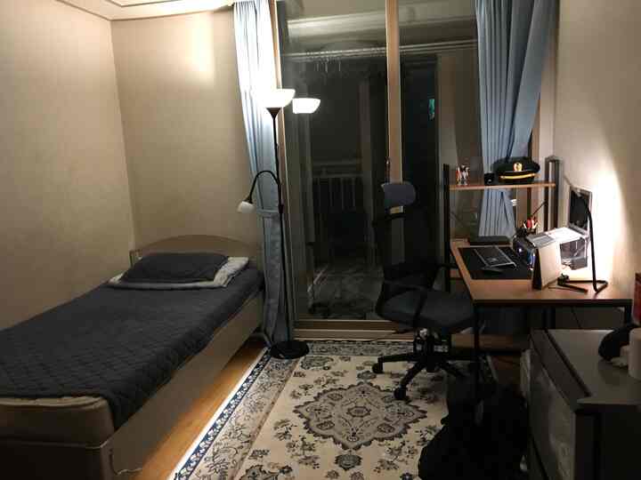 White and blue toned studio bedroom featuring bed, desk, and office chair arranged in a neat home office space
