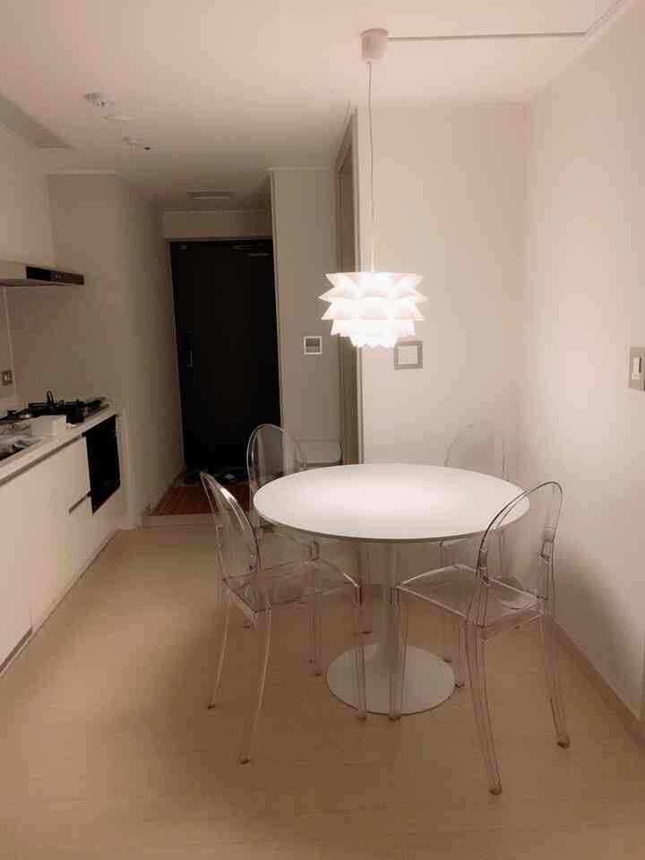 白と透明素材が調和する縦長のキッチン、円形テーブルとゴーストチェアが配置されたシンプルモダンなホームカフェ空間