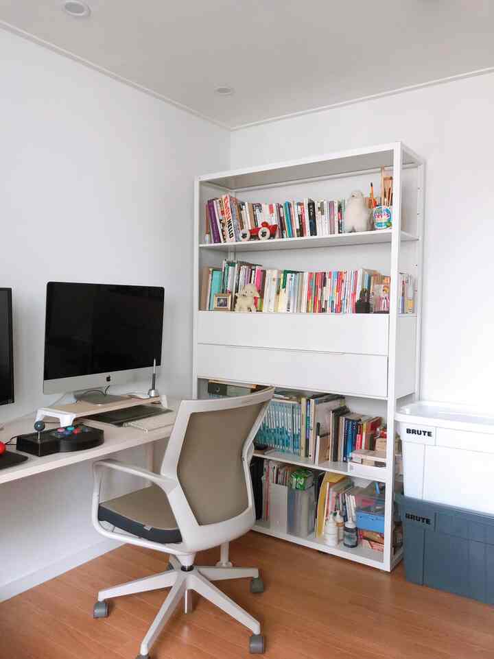 Compact game and work room in white and brown tones, featuring monitor setup and bookshelf with clean atmosphere