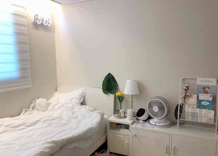 Bright white-toned bedroom featuring white bed, nightstand, and cabinet with a clean, natural atmosphere