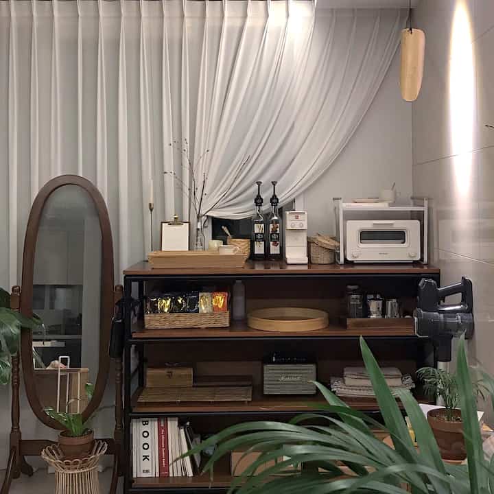 Wood tone and white curtains define this home cafe space featuring a coffee machine and trays with an inviting warm atmosphere