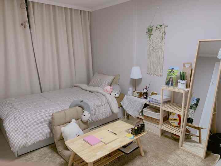 Beige and natural tone bedroom featuring a single bed, wooden desk, full-length mirror, and shelves creating a warm, cozy atmosphere