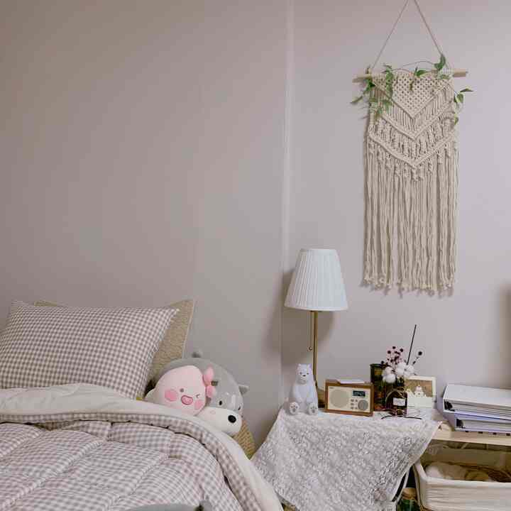 Beige and white toned bedroom featuring checkered bedding, macrame wall hanging, and plush toys arranged in a cozy style