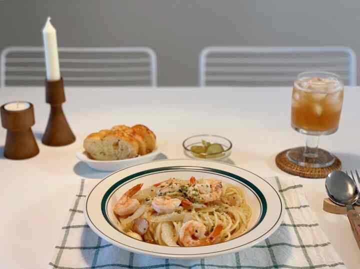 White and natural tone dining table featuring shrimp pasta and iced drink, creating a cozy space for eating alone.