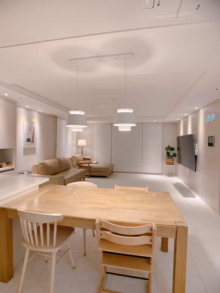 A white and beige toned living room featuring a wooden dining table and sofa with a modern natural atmosphere