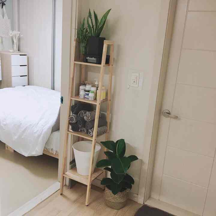 白と木目調が調和する寝室のトイレ入口の棚スペース、タオルと植物がきれいに整えられた落ち着いた雰囲気のインテリア