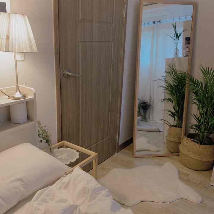 Natural wood tone and white bedroom featuring a side table, full-length mirror, and plants, creating a cozy and simple atmosphere