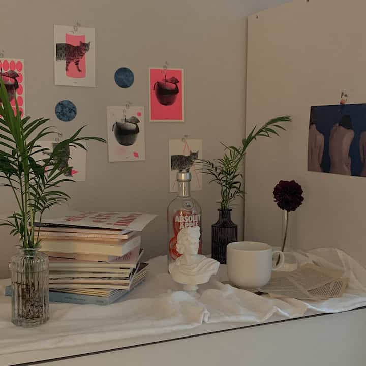 White and gray toned interior featuring a plaster bust, vases with plants, and wall art including cats and apples, conveying a minimalist vibe