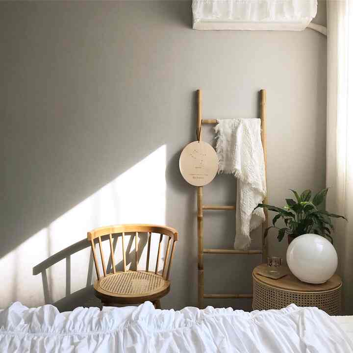 Cozy bedroom with warm wood tones and white elements, featuring a cane chair and nightstand bathed in natural light