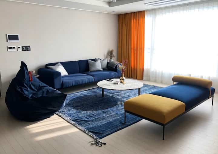 Living room with navy sofa and orange curtains, featuring coffee table and bean bag in a modern styled, clean space