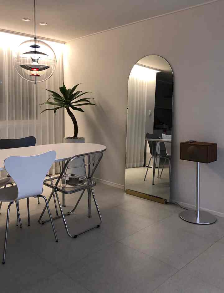 White and natural tone dining room featuring a white dining table and chairs, an arched wall mirror, and a green plant creating a clean, atmospheric space