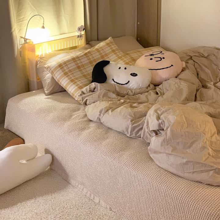 Cozy bedroom in warm beige and brown tones featuring a bed centered with Snoopy and Charlie cushions