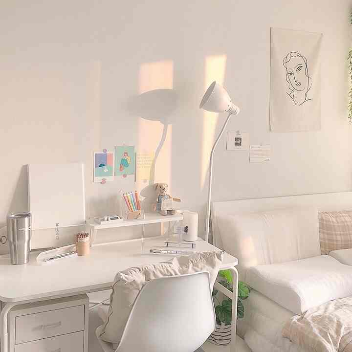 白とベージュのトーンが特徴のワンルームホームオフィス、机とフロアランプ、ソファベッドが配置された雰囲気のある空間