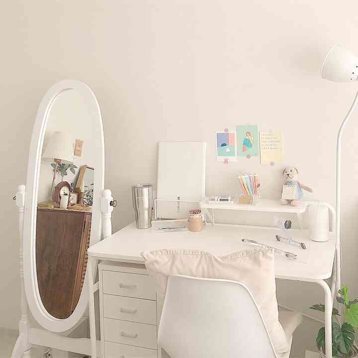 Natural and white toned studio apartment home office featuring a desk, full-length mirror, and cushioned chair creating a cozy atmosphere