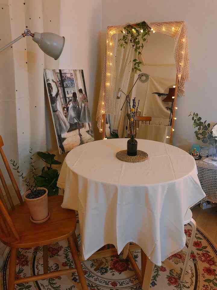 Light beige toned small apartment living room featuring a round table, Persian rug, vase, and cozy lighting with plants