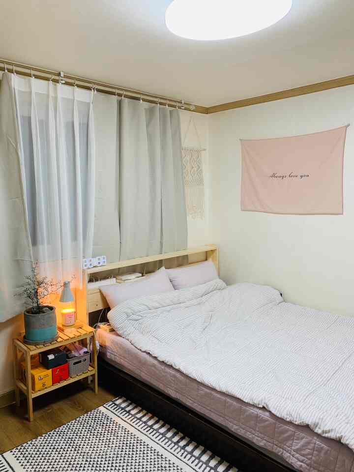 Soft beige and white bedroom featuring a wooden bed headboard and shelf, blackout curtains, and macrame wall hanging creating a harmonious space