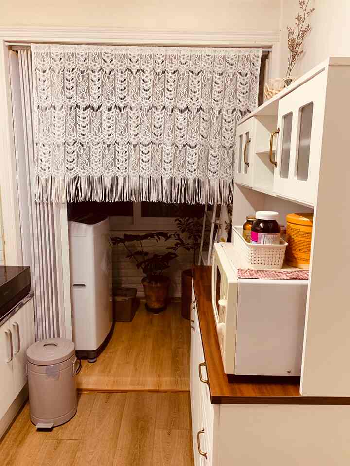 Narrow kitchen space featuring warm brown wood tone flooring and white cabinetry with lace room divider curtain at entrance