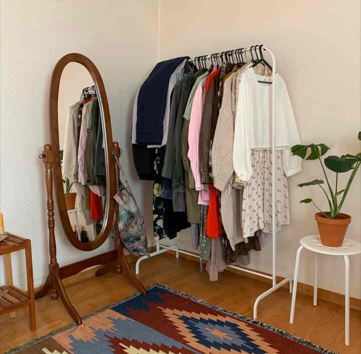 白い壁と木製の全身鏡、ハンガーラックが配置されたヴィンテージ風のワンルームウォークインクローゼット