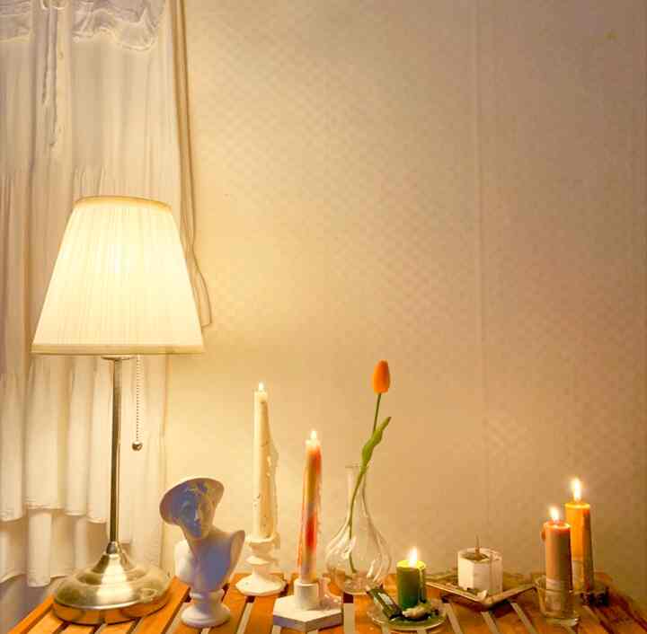 Cozy room with warm orange and white tones featuring candles, plaster statue on a wooden shelf creating a mood ambiance