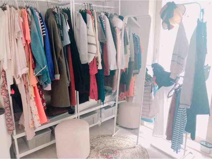 ホワイトとベージュの色調のウォークインクローゼット、衣類ハンガーとスツールが配置された明るく居心地の良いインテリア