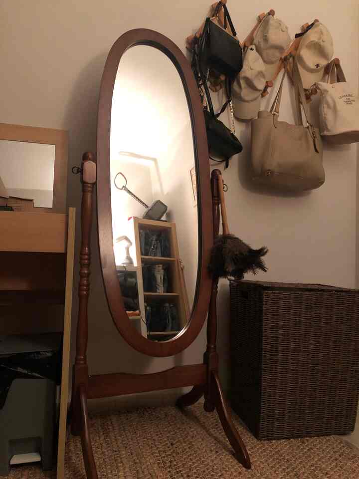 Walk-in closet space dominated by wood tone and brown colors, featuring a large oval full-length mirror center, rattan hamper, and woven rug creating a cozy wardrobe room atmosphere