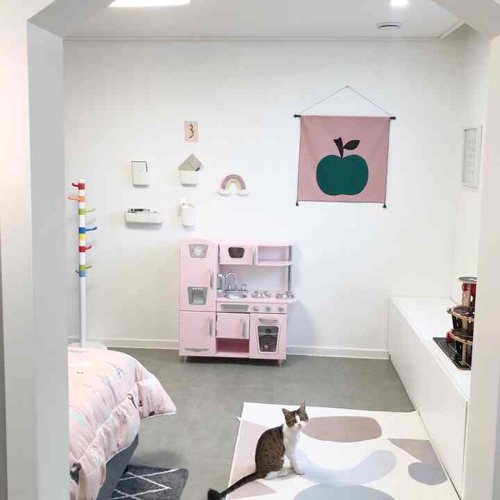 Bright and clean kids' room in white and pink tones featuring a pink play kitchen and fabric wall art