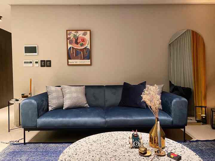 ベージュの壁と濃いブルーのソファ、ゴールドのアクセントがあるモダンなリビング