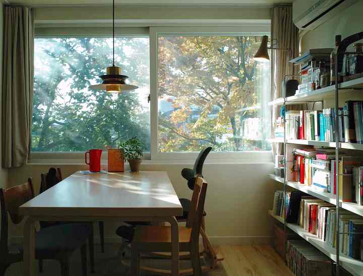 Natural wood tone and beige study-like living room featuring a large dining table and bookshelf with soft natural lighting