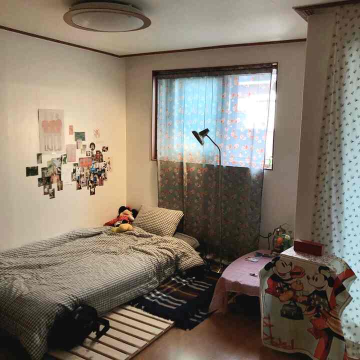Soft beige-toned studio bedroom with a checkered bed, floral curtains, and cozy Disney fabric decorations