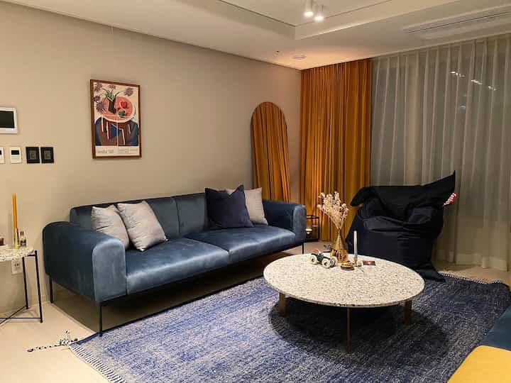 Blue and gold toned living room featuring modern sofa, round coffee table, and hotel-style curtains in a sophisticated space