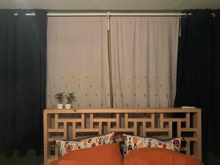 ナチュラルな木目調の寝室、ネイビーの遮光カーテンとオレンジの寝具が調和した落ち着いた空間