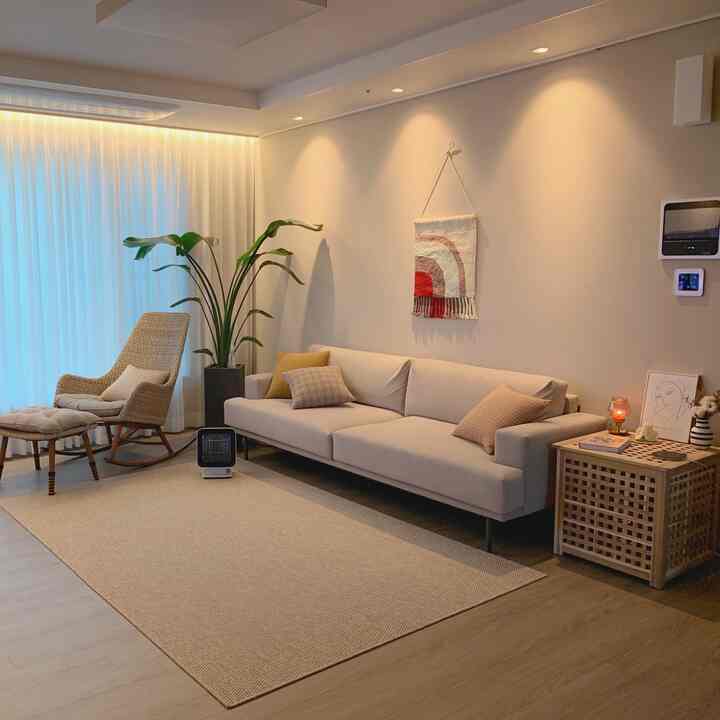 ベージュとナチュラルウッドトーンのリビング、ラタンのロッキングチェアとホワイトカーテンが配置された落ち着いた空間