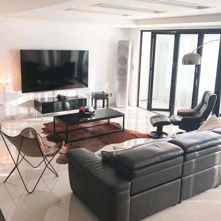 Bright-toned living room with black furniture featuring large TV, recliner chair, and cowhide rug in a modern setting