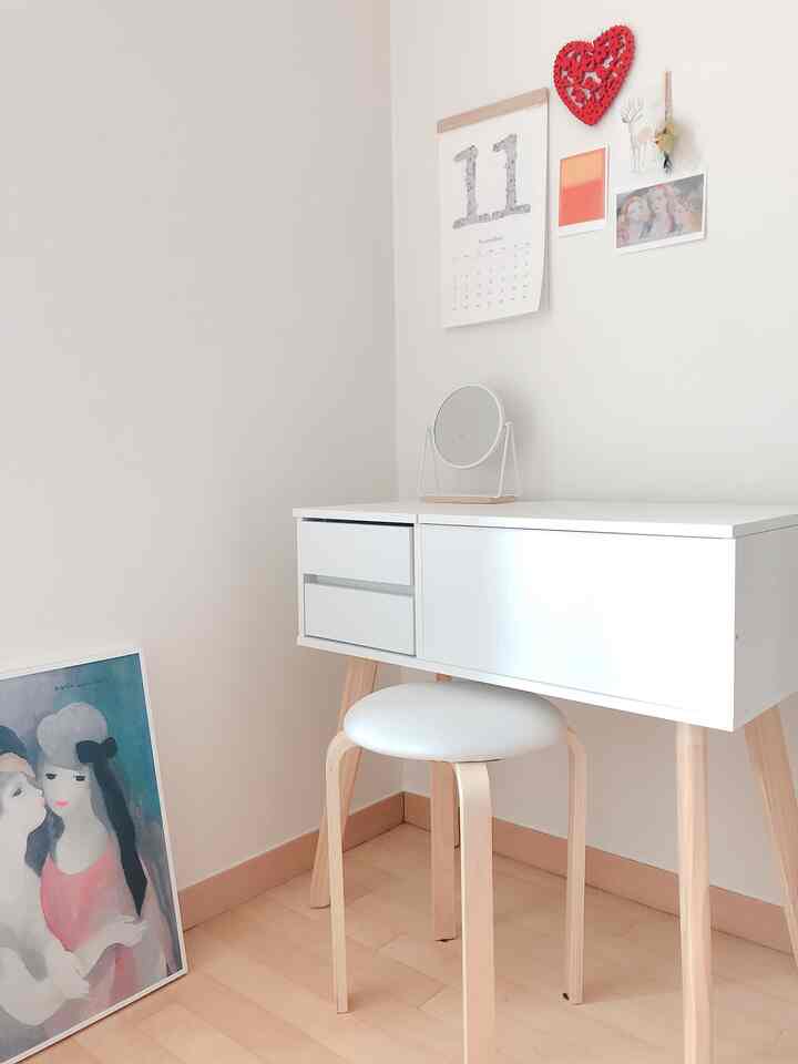 Simple corner vanity and wooden stool in a small room with white and wood tones