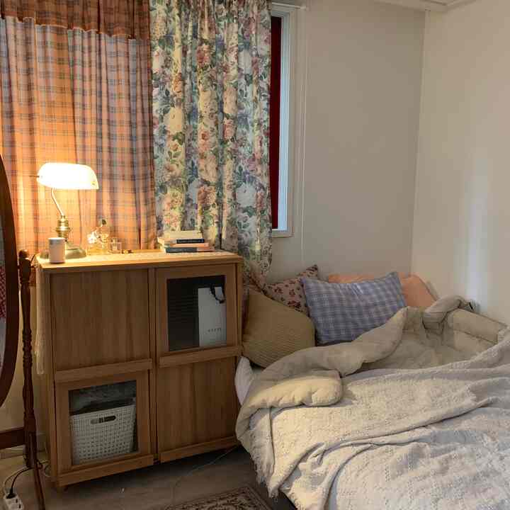 ベージュと木目調が調和した居心地の良い寝室、チェック柄と花柄のカーテン、木製キャビネットが配置された雰囲気のあるインテリア